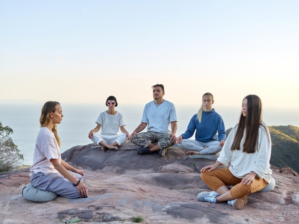 a group of campers and yoga enthusiasts performing a group meditation sessions early during a morning hike at the top of a mountain
